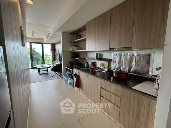 Modern kitchen with sleek wooden cabinets and open layout leading to a bright living area.