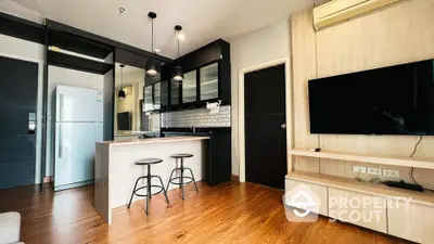 Modern kitchen with sleek black cabinets, breakfast bar, and cozy living area with mounted TV.