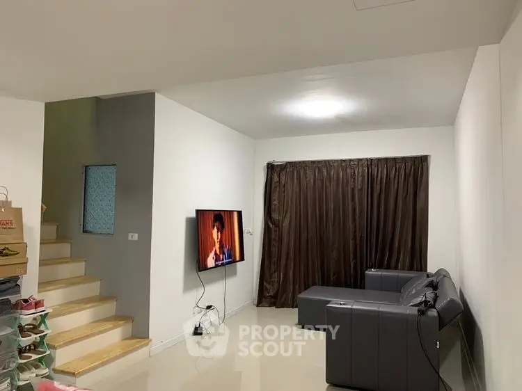 Modern living room with sleek gray sofa and wall-mounted TV, featuring minimalist design and cozy ambiance.