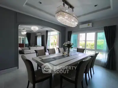 Luxurious dining room with elegant chandelier and large windows offering garden views.