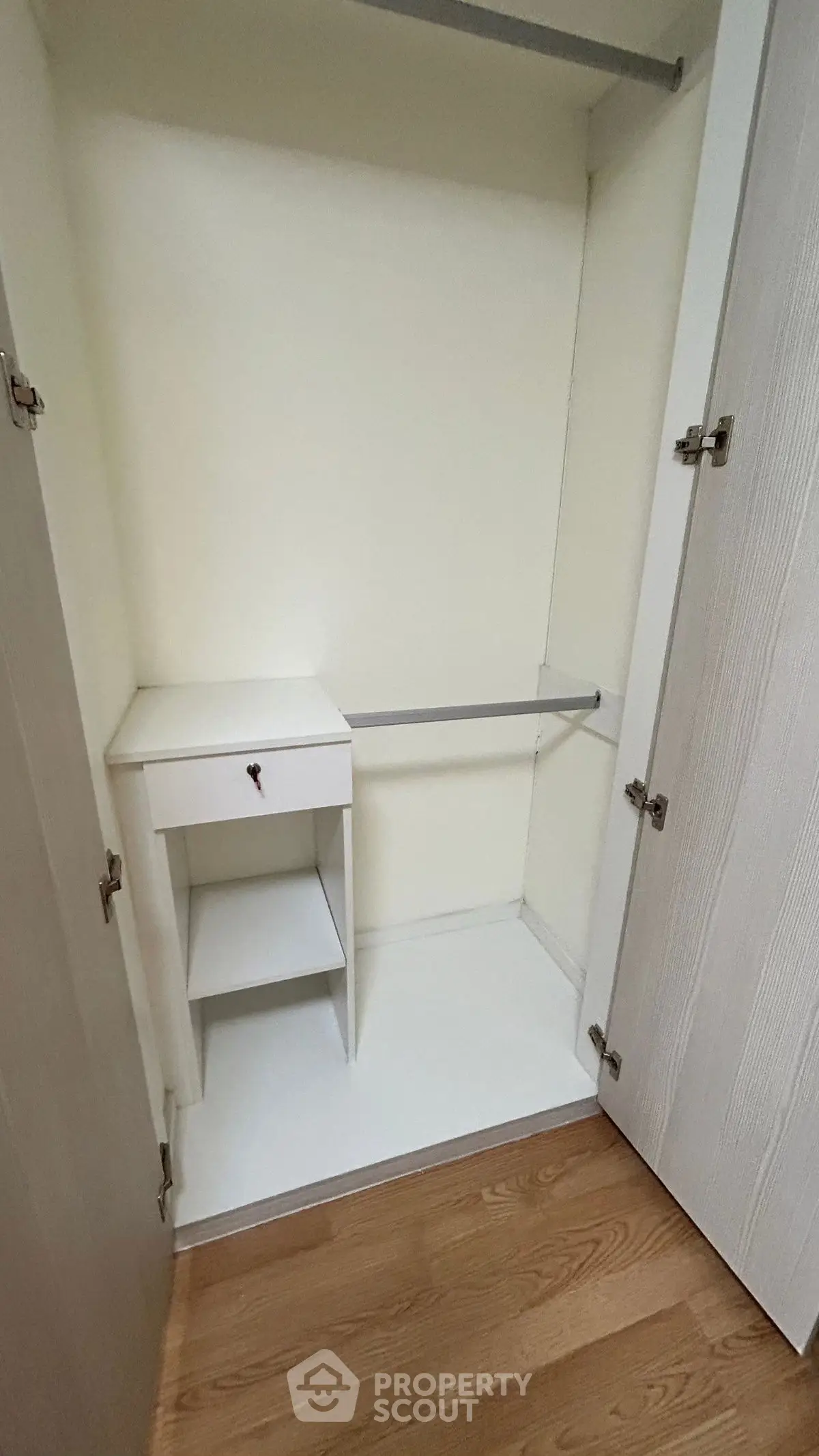 Spacious white closet with wooden flooring, featuring a small built-in drawer and shelf.