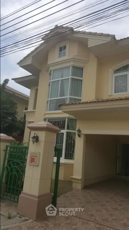 Elegant two-story house with large windows and gated entrance in a serene neighborhood.