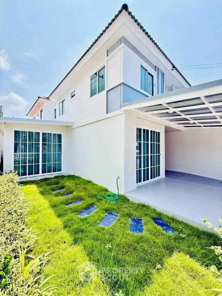 Modern two-story house with lush green lawn and spacious carport in a sunny setting.