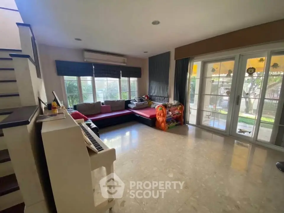 Spacious living room with large windows and garden view, featuring a cozy sofa and piano.