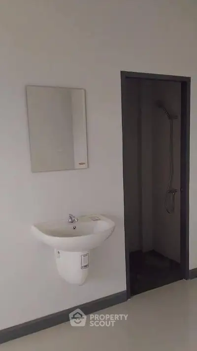 Minimalist bathroom with wall-mounted sink and shower area in modern apartment.