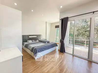 Spacious bedroom with large windows and balcony access, featuring modern decor and natural light.
