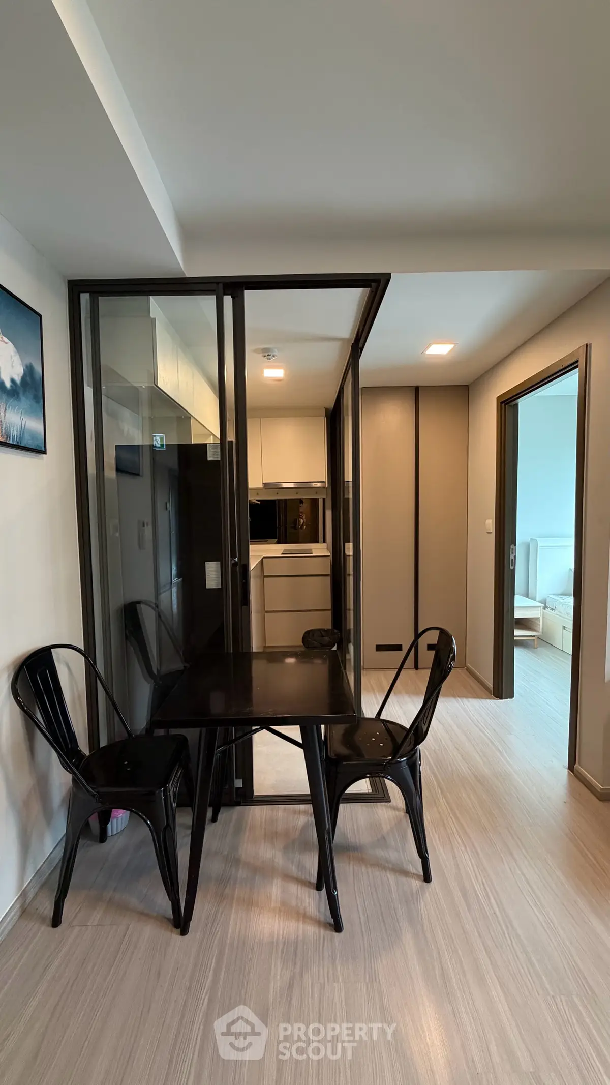 Modern apartment interior with open kitchen and dining area featuring sleek black chairs and wooden flooring.