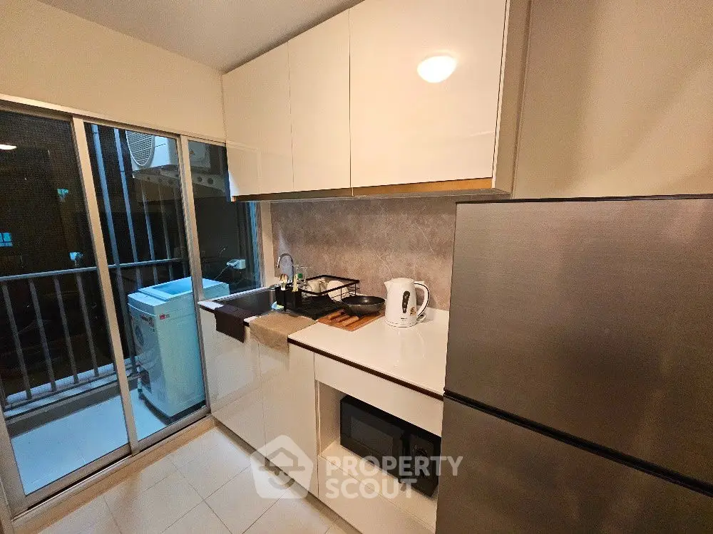 Modern kitchen with sleek appliances and balcony view, featuring a washing machine and stainless steel fridge.