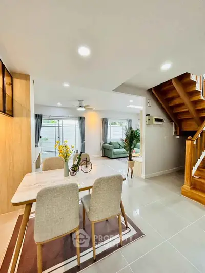 Modern open-plan living and dining area with stylish decor and wooden staircase.