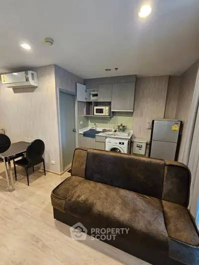 Modern apartment with compact kitchen and cozy living area, featuring washing machine and microwave.