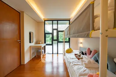 Modern bedroom with bunk bed and natural light, featuring a cozy workspace and wooden flooring.