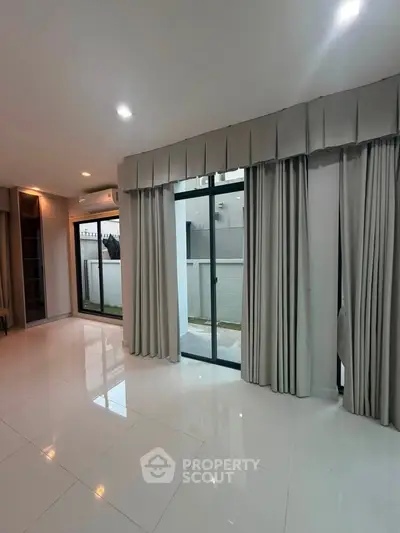 Spacious modern living room with large windows and elegant curtains, perfect for natural light.