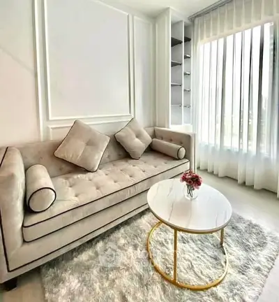Elegant living room with plush sofa, chic coffee table, and natural light through sheer curtains.