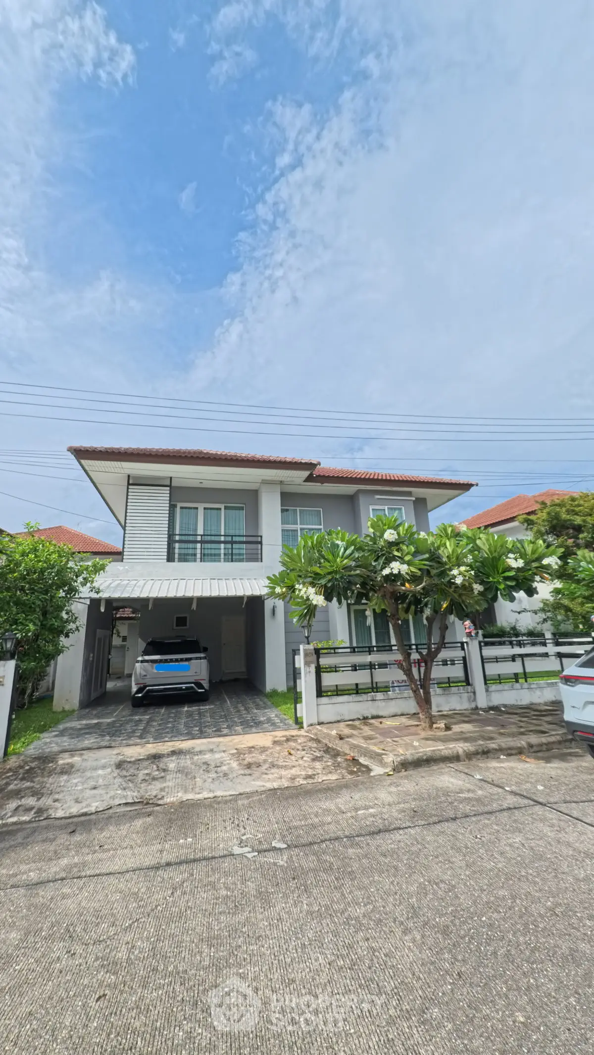 Charming two-story house with carport and lush greenery in a serene neighborhood.