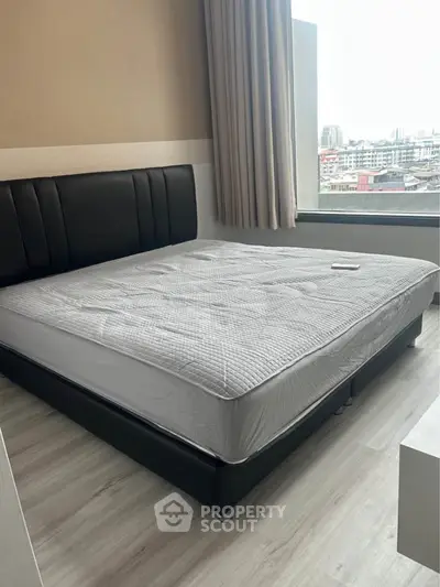 Spacious bedroom with large window offering city views, featuring a modern bed and sleek flooring.