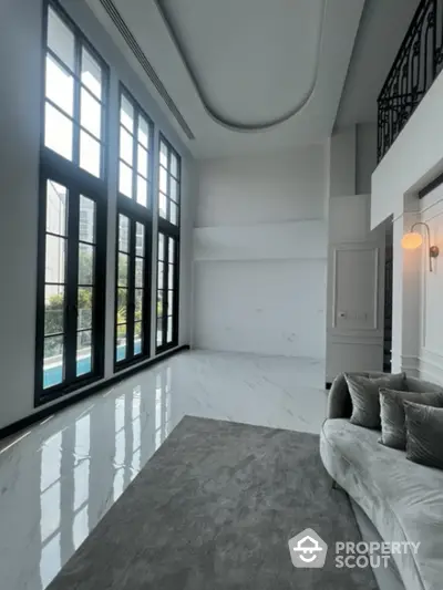 Luxurious high-ceiling living room with gleaming marble floors and towering windows offering abundant natural light, leading to a serene outdoor view.