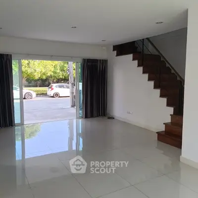 Spacious living room with glossy tile flooring and staircase, featuring large sliding glass doors opening to a serene view.