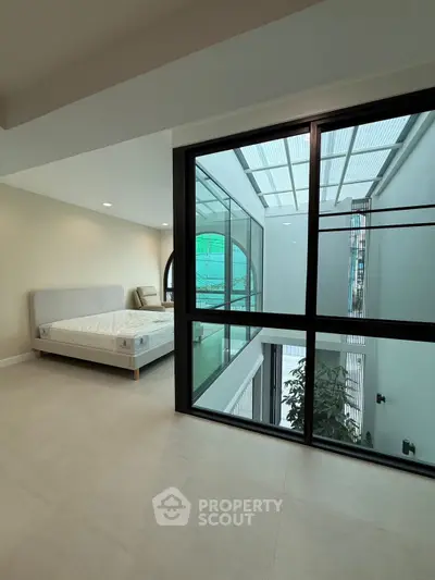 Modern bedroom with large window overlooking an atrium, featuring a minimalist bed and neutral decor.
