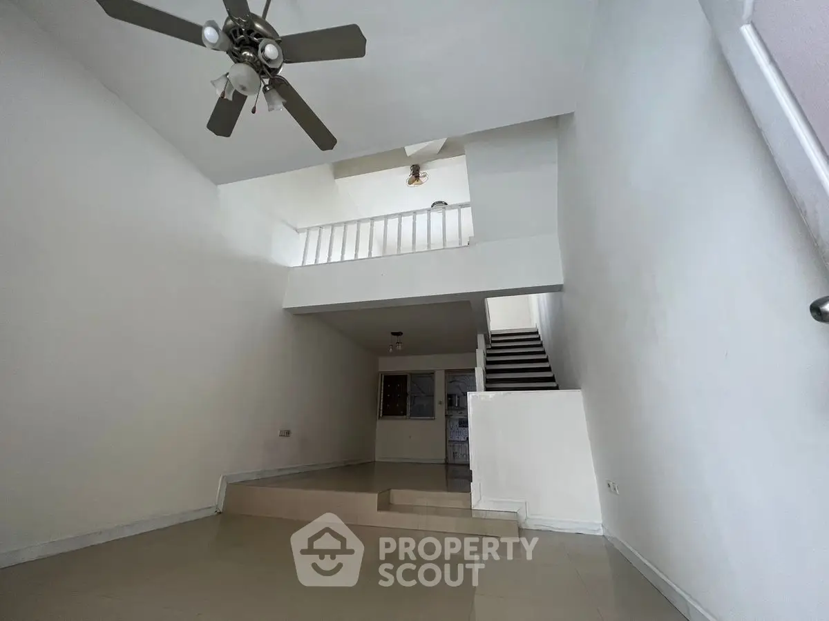 Spacious two-story living room with modern ceiling fan and sleek staircase.