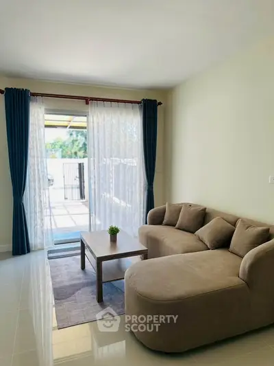 Spacious living room with modern sofa and large window leading to balcony, perfect for relaxation.
