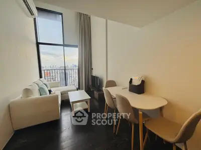 Modern living room with high ceilings and city view, featuring a cozy sofa and dining area.