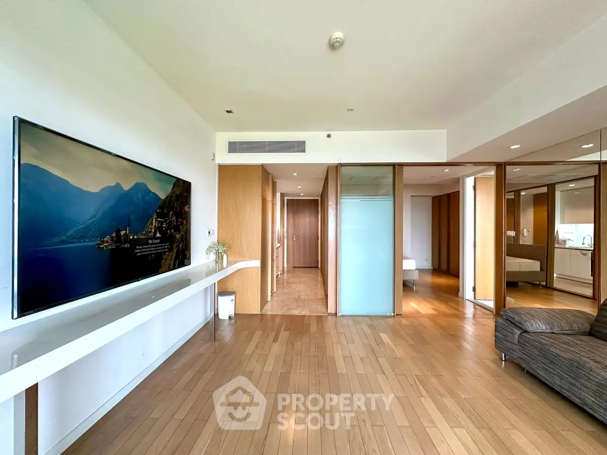 Spacious modern living room with wooden flooring and large TV, perfect for relaxation.