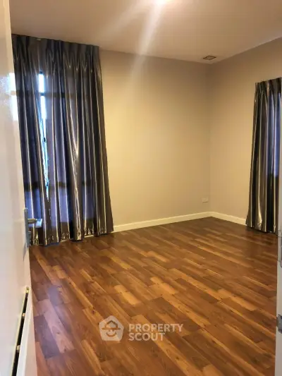 Spacious empty room with elegant wooden flooring and large windows with curtains.