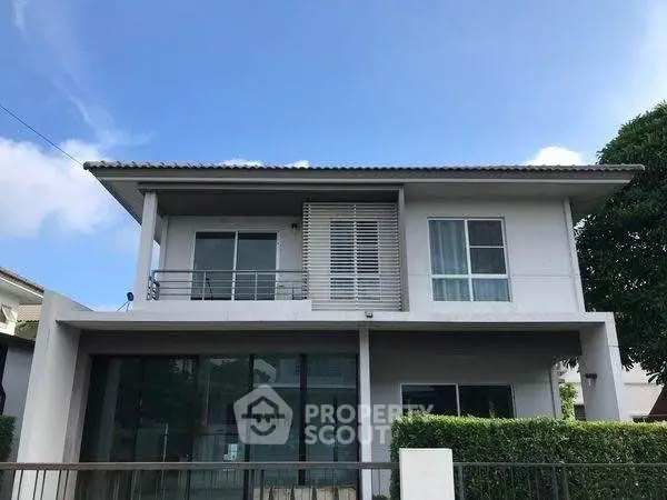 Modern two-story house with balcony and large windows in a serene neighborhood.