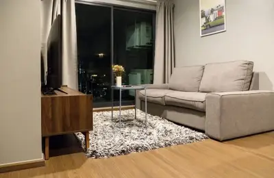 Modern living room with cozy sofa, stylish rug, and large window with city view.