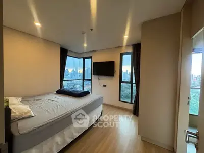 Modern bedroom with city view and large windows, featuring a cozy bed and mounted TV.
