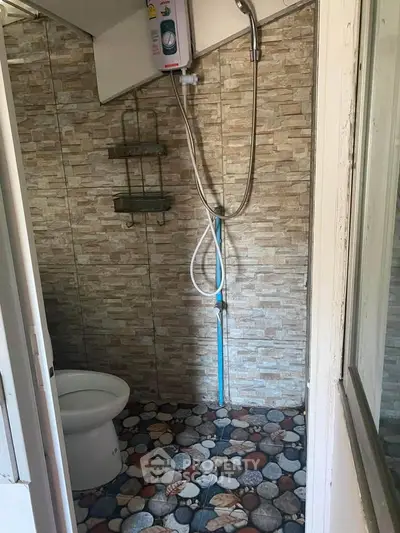 Compact bathroom with stone tile flooring and wall-mounted shower in cozy real estate unit.