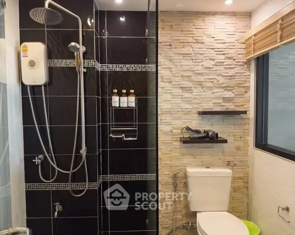 Modern bathroom with sleek black tiles and stone accent wall, featuring a shower and toilet.