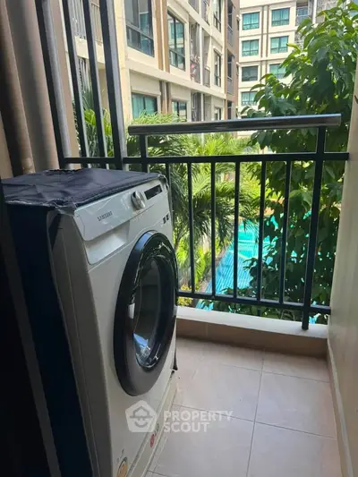 Charming balcony with washing machine overlooking lush greenery and pool view in modern apartment complex.