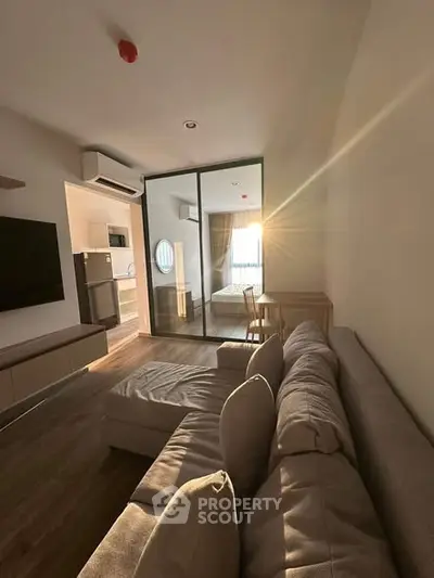 Modern living room with cozy sofa and sunlight streaming through glass doors to bedroom.