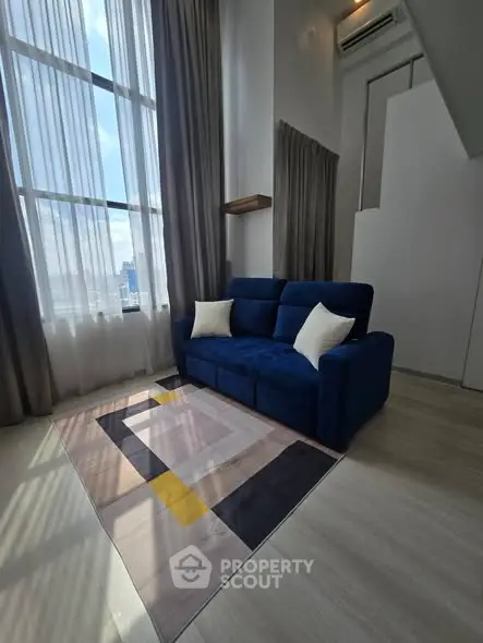 Modern living room with high ceilings and large windows, featuring a stylish blue sofa and elegant decor.