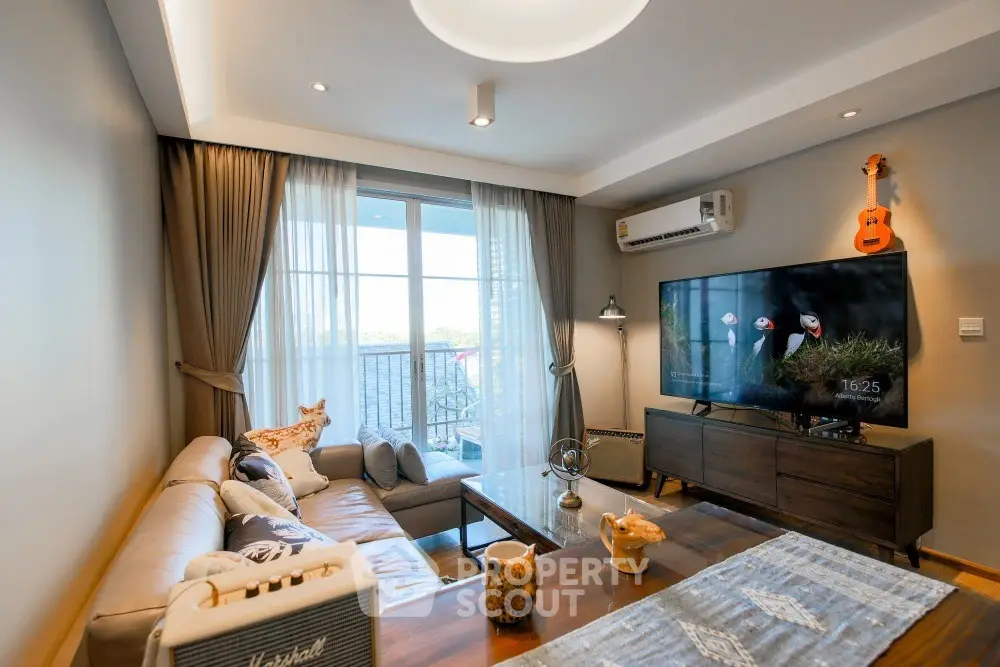Stylish living room with modern decor, large TV, and balcony access in a cozy apartment.