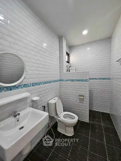 Modern bathroom with white tiles and sleek fixtures, featuring a round mirror and contemporary design.