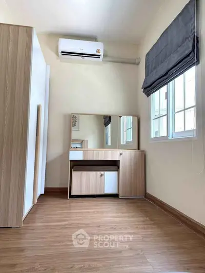 Spacious bedroom with wooden flooring and modern furniture, featuring a large window and air conditioning.