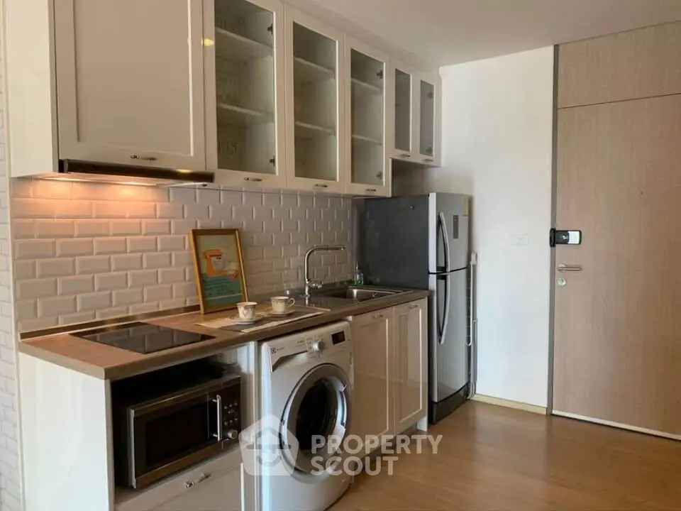 Modern kitchen with washing machine, fridge, and microwave in compact layout.