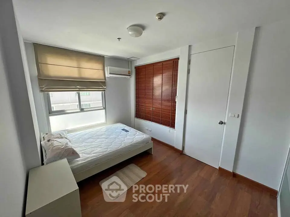 Cozy bedroom with wooden flooring and ample natural light, featuring a comfortable bed and modern window blinds.