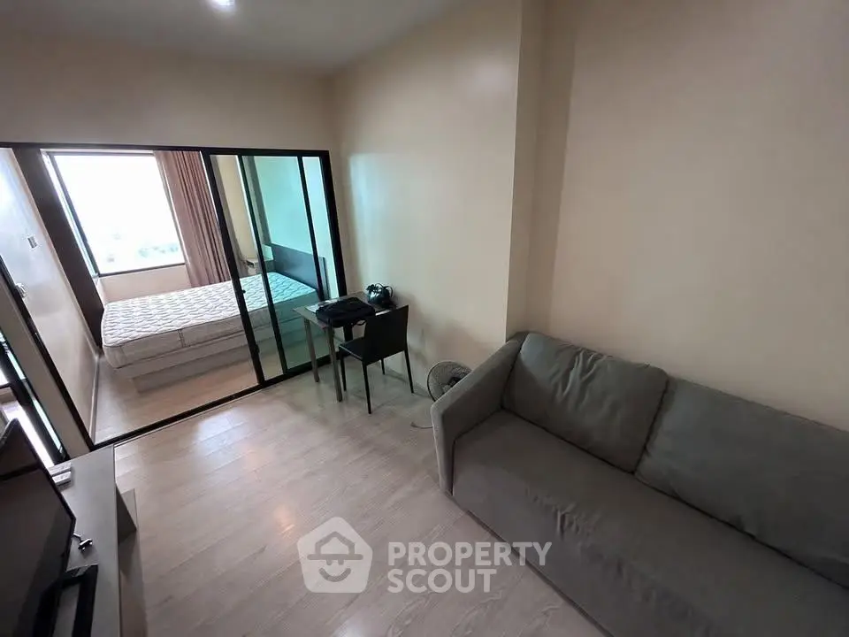Modern apartment with cozy living room and bedroom, featuring sleek glass partition and stylish furnishings.