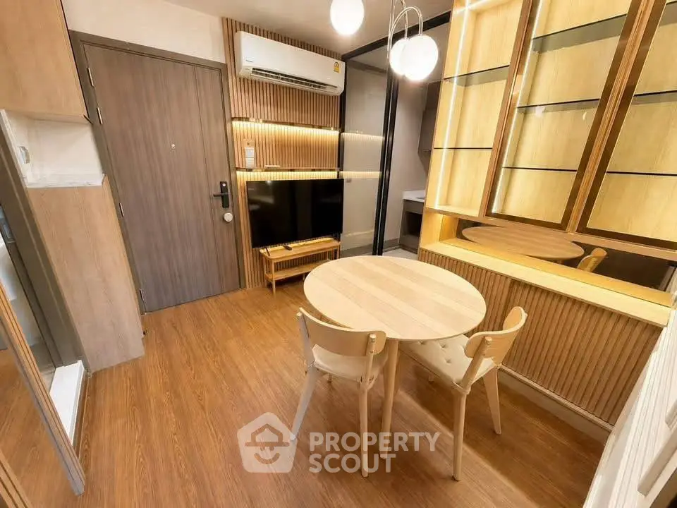 Modern apartment interior with wooden flooring, dining table, and TV setup.