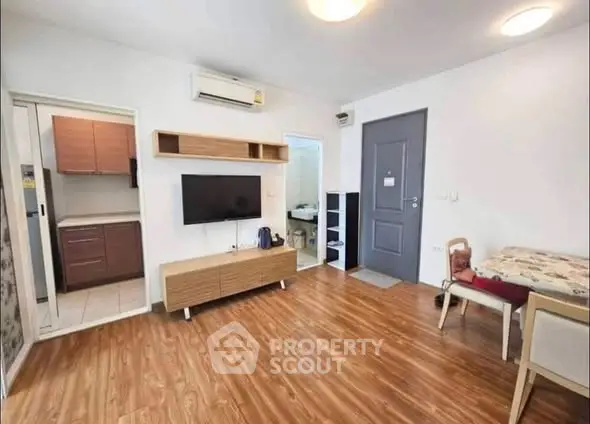 Modern living room with wooden flooring, wall-mounted TV, and open kitchen layout.