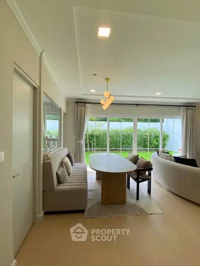 Spacious living room with modern decor and garden view, featuring elegant lighting and large windows.