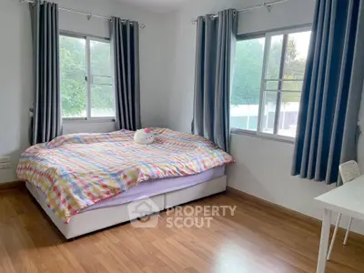 Bright bedroom with large windows and cozy bed, featuring wooden flooring and modern curtains.