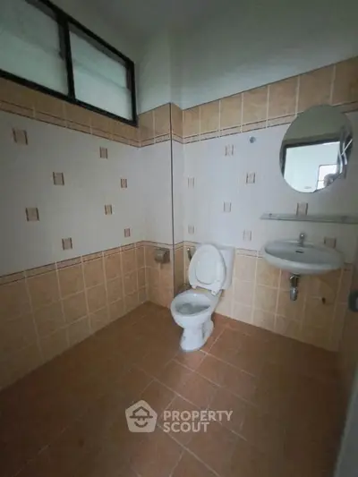 Spacious bathroom with tiled walls and floor, featuring a toilet and sink.