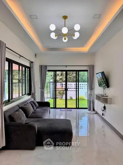 Modern living room with large windows and stylish chandelier, offering a view of the garden.