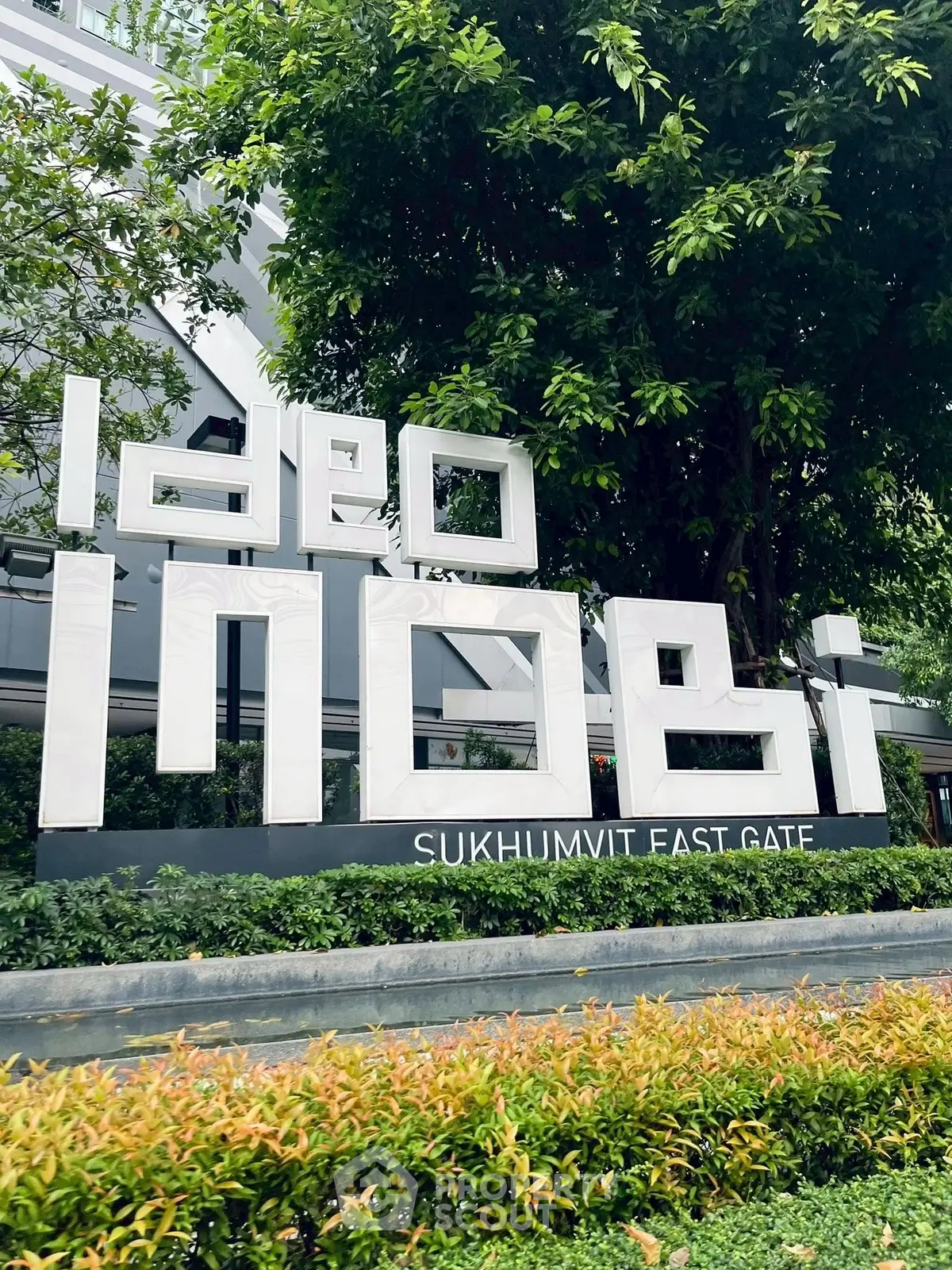 Modern building entrance with sleek signage at Sukhumvit East Gate, surrounded by lush greenery.