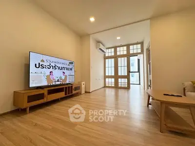 Spacious modern living room with wooden flooring and large TV, perfect for relaxation.