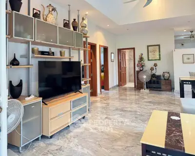 Spacious living room with modern decor and marble flooring, featuring a large TV and stylish shelving.